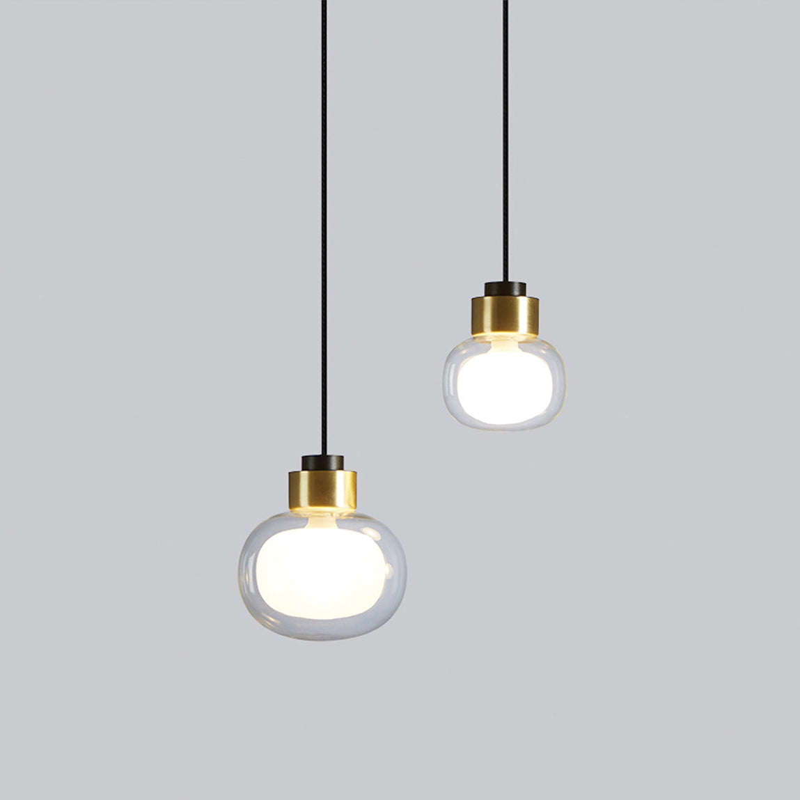 Two Clérachic glass pendants with gold collars hang at different heights, the larger size lower, against a light grey backdrop.