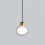 A single Clérachic glass pendant with a gold collar and a frosted inner glow, hanging against a plain light grey backdrop.