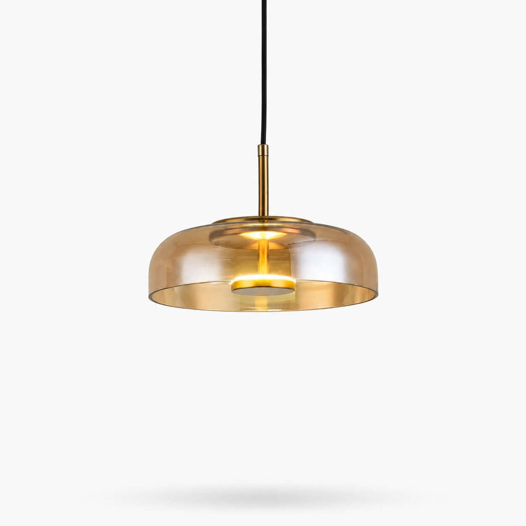 Amber glass Clérachic pendant light on a white backdrop, a wide shallow dome with a brass stem and a lit LED disc inside.