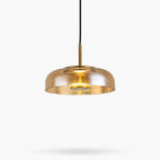 Amber glass Clérachic pendant light on a white backdrop, a wide shallow dome with a brass stem and a lit LED disc inside.
