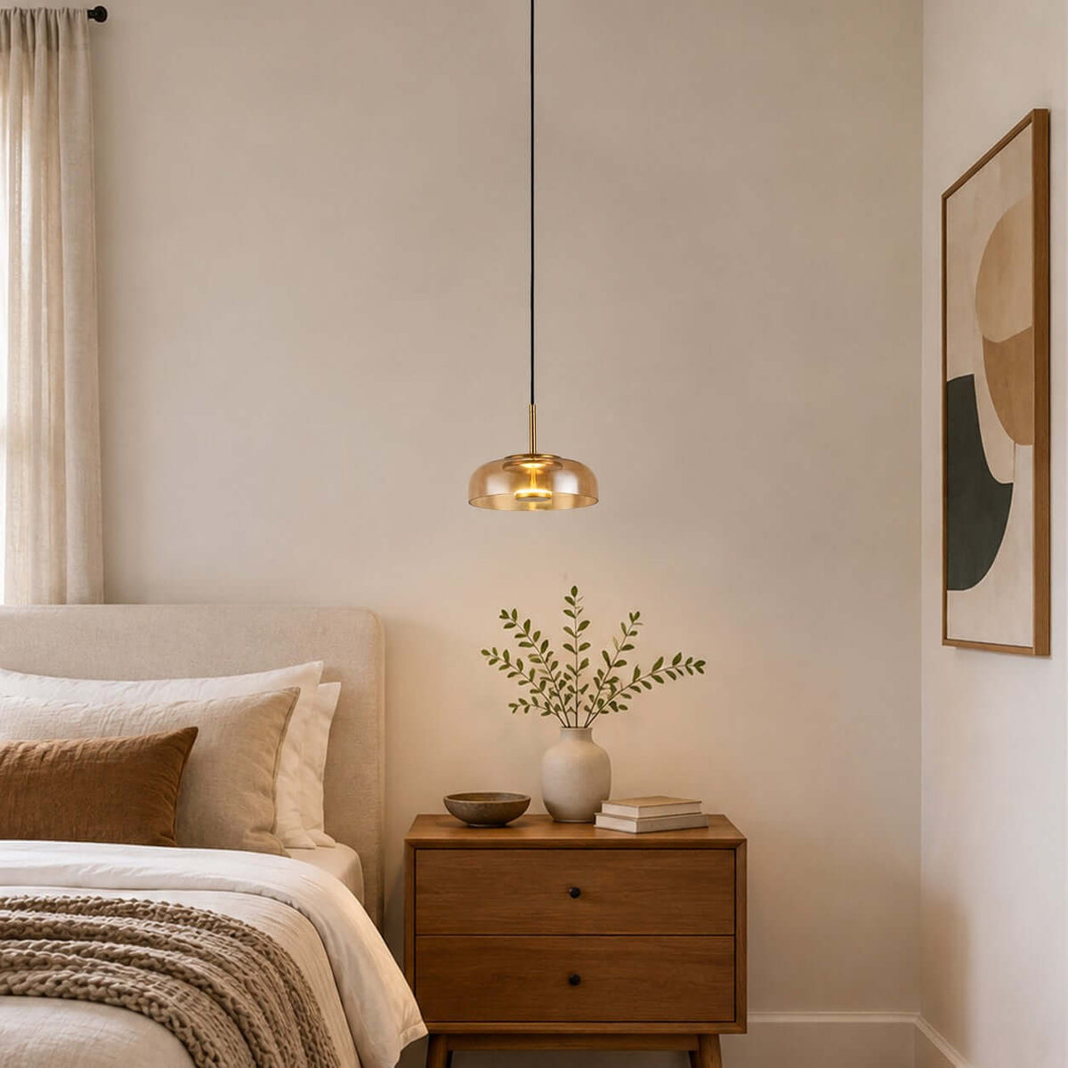 Lit amber glass Clérachic pendant light in a bedroom corner, above a walnut chest of drawers and a framed abstract print.