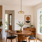 Amber glass Clérachic pendant light above a round table in a dining nook, with a sideboard and an abstract print behind it.