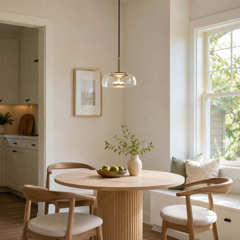 Clear glass Clérachic pendant light over a small round table by a sunny window, with bentwood chairs and a bowl of green fruit.