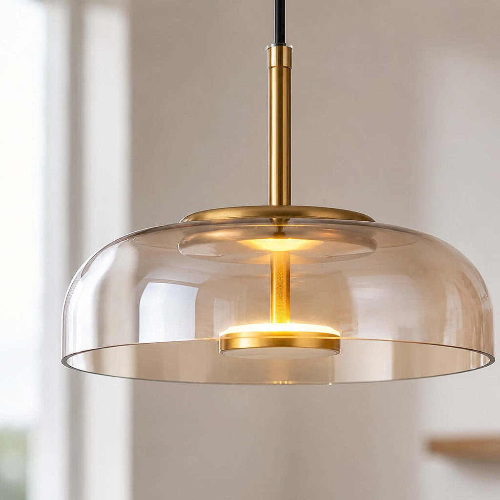 Close view of an amber glass Clérachic pendant light, its brass stem and glowing LED disc seen through the rounded glass.