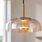 Close view of an amber glass Clérachic pendant light, its brass stem and glowing LED disc seen through the rounded glass.