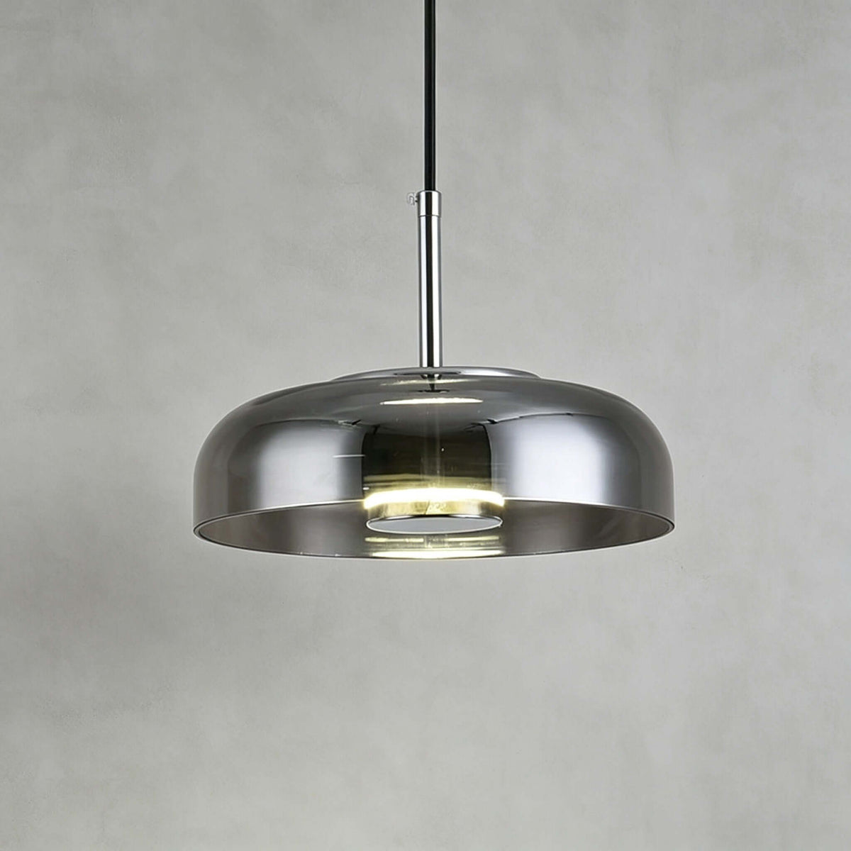 Smoke grey glass Clérachic pendant light against a grey plaster wall, its silver-toned stem and lit disc visible inside.