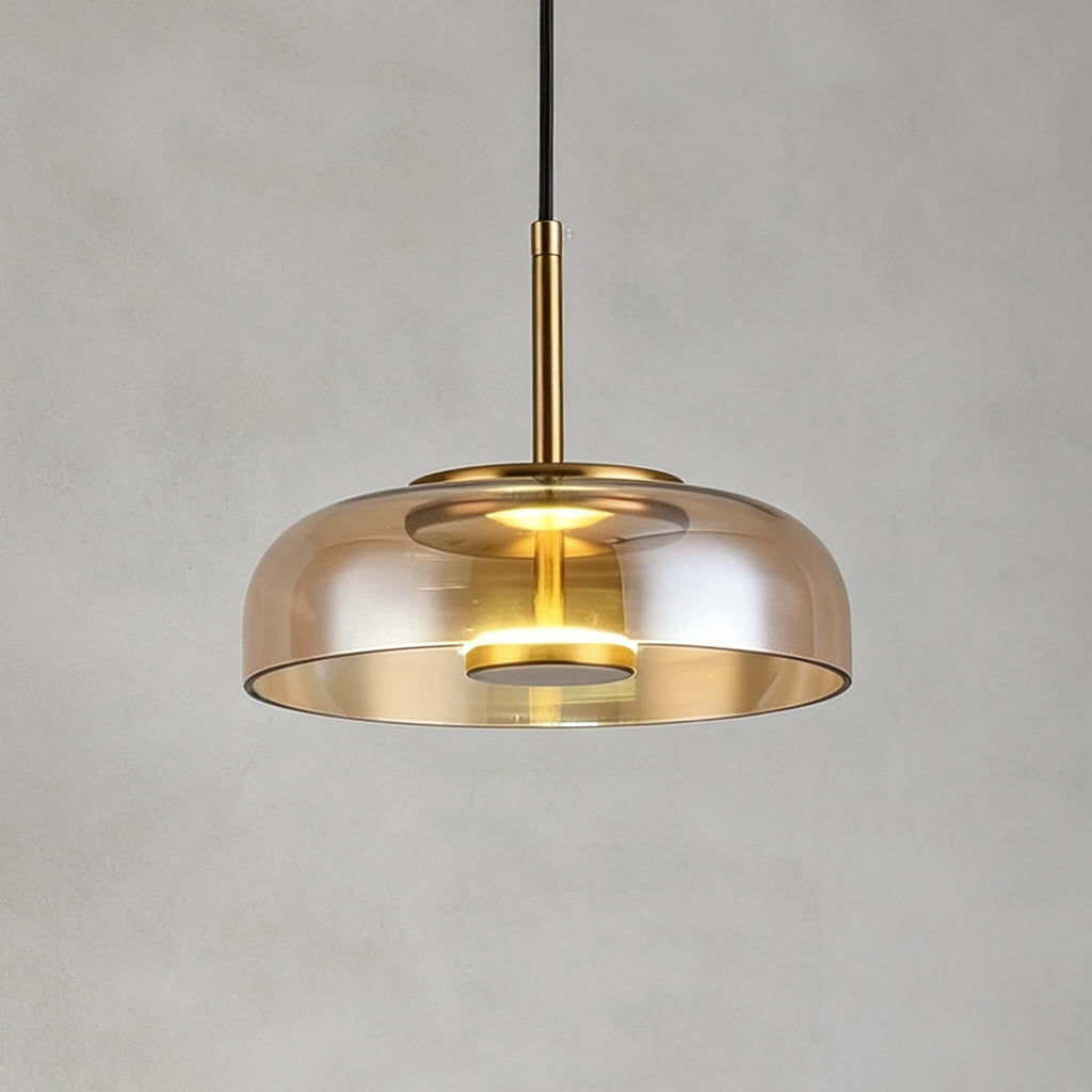 Amber glass Clérachic pendant light on a grey backdrop, a brass stem rising from a lit disc inside the shade.