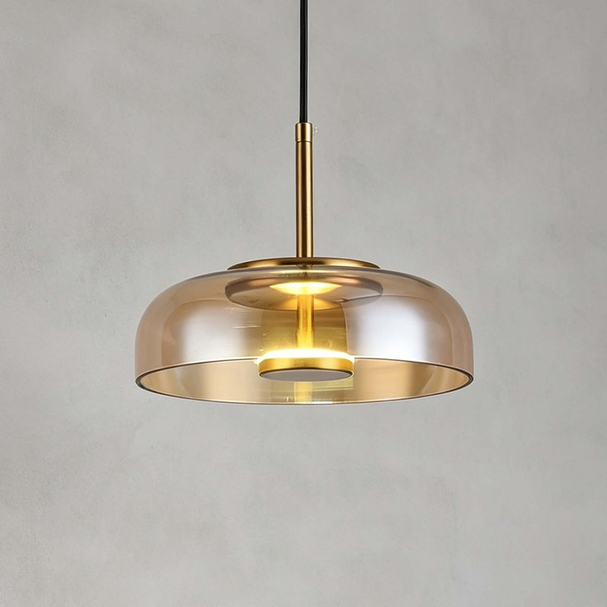 Amber glass Clérachic pendant light on a grey backdrop, a brass stem rising from a lit disc inside the shade.