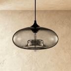 Clérachic pendant light, unlit, with a smoked-grey oval glass shade, black cord and cap, and a clear tube bulb inside.