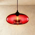 Clérachic pendant light with a glowing red blown-glass oval shade, black cap and cord, and a warm tube bulb inside.