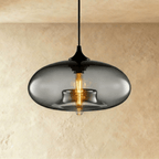 Clérachic pendant light with a smoked-grey oval glass shade lit by an amber tube bulb, black cord and cap above.