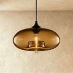 Clérachic pendant light with a coffee-brown glass oval shade, glowing tube bulb inside and a slim black cord and cap.