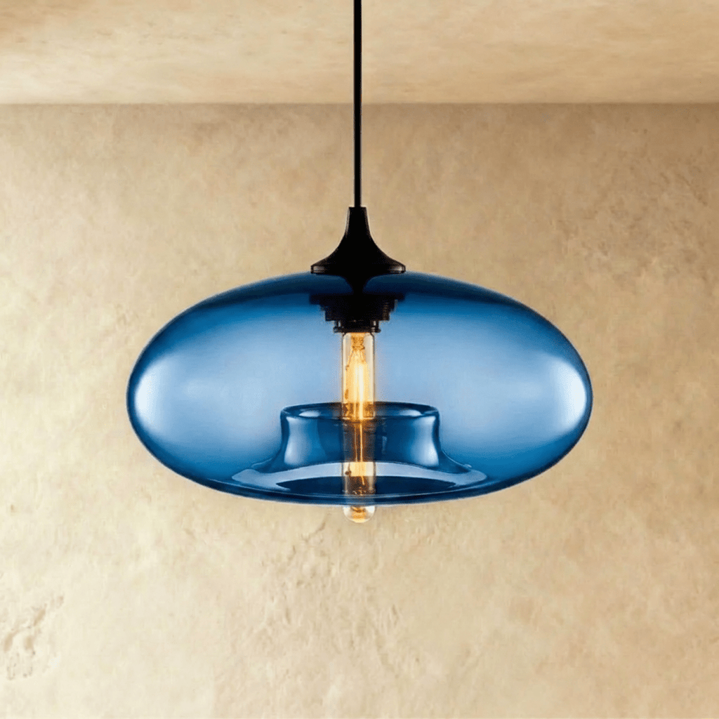 Clérachic pendant light with a deep blue blown-glass oval shade, black cap and cord, and a warm filament bulb inside.