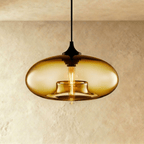 Clérachic pendant light with a golden amber oval glass shade, black cap and cord, and a lit tube bulb in the centre.