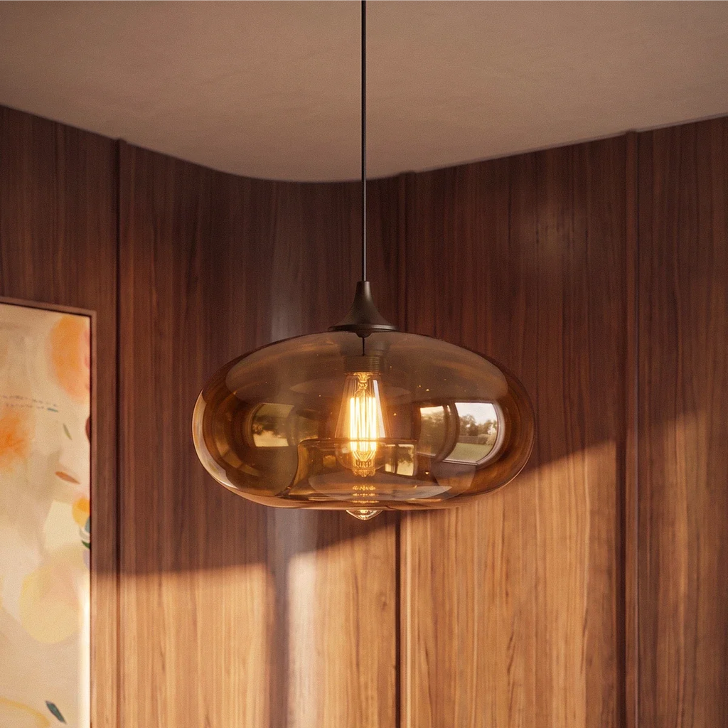 Clérachic amber-brown glass pendant light with a lit filament bulb, hung against walnut wall panels and a soft curved ceiling.
