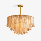 A Clérachic tiered pendant of ribbed glass leaves in amber, hung from a brass rod and ceiling plate on a plain white backdrop.