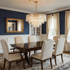 A Clérachic glass leaf pendant hangs in a dining room with navy walls, cream chairs and a gold-framed mirror.