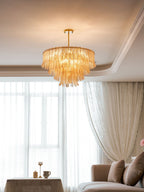 A Clérachic amber leaf-glass pendant glows below a coved white ceiling, with a window of sheer curtains and a sofa below.