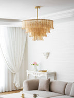 A Clérachic amber leaf-glass pendant hangs in a white living room, with a sofa, a carved console and pink flowers beyond.