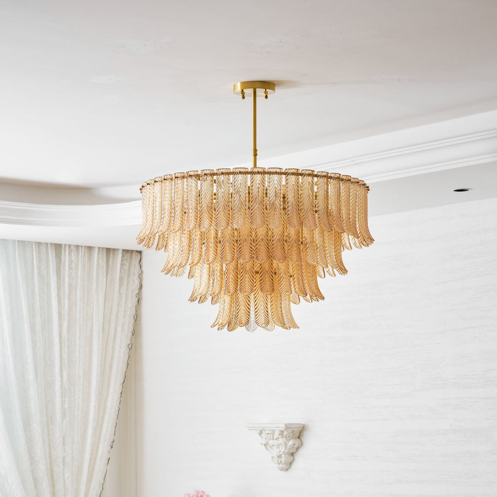 A Clérachic pendant with three tiers of amber ribbed glass leaves hangs from a brass rod below a white ceiling.