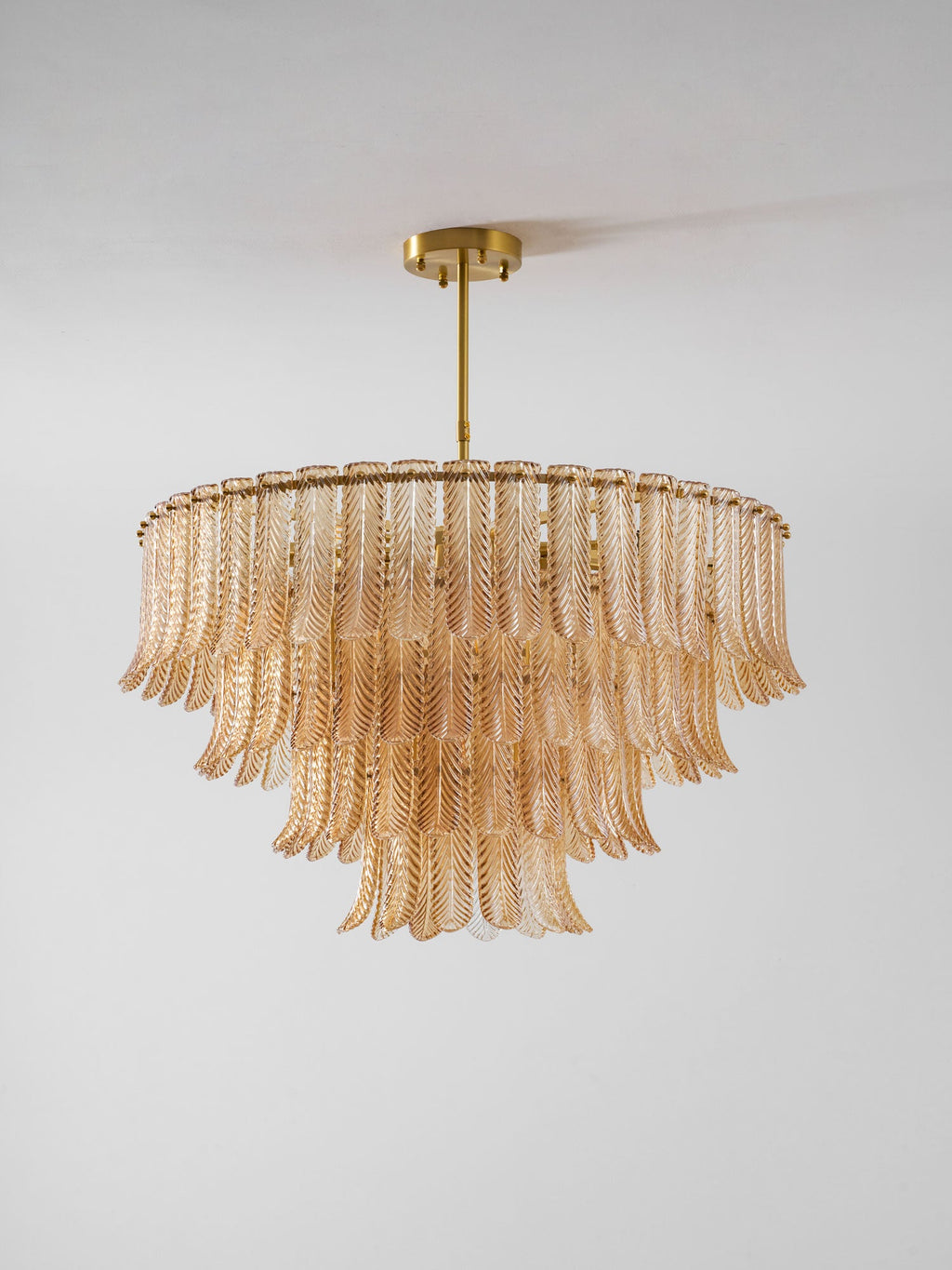 A Clérachic pendant with tiers of amber ribbed glass leaves on a round brass frame, hanging against a pale grey wall.