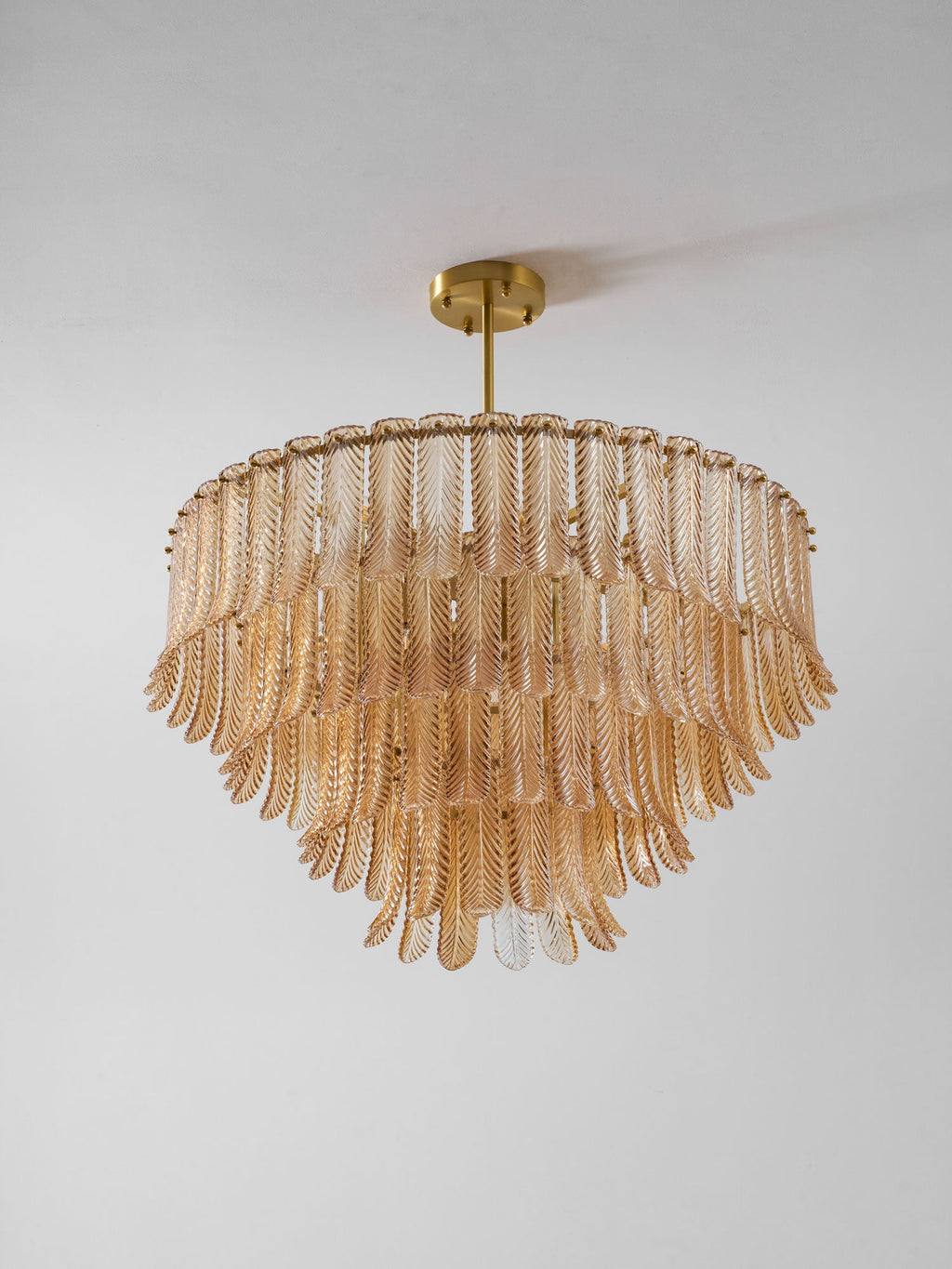 A Clérachic pendant with tiers of amber glass leaves on a round brass ring, hung from a short brass stem on a grey backdrop.