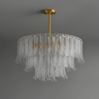 A Clérachic pendant of clear glass leaves in layered tiers hangs from a brass rod, shown against a mid-grey backdrop.
