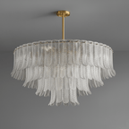 A wide Clérachic pendant with three tiers of clear ribbed glass leaves hangs from a brass rod against grey.
