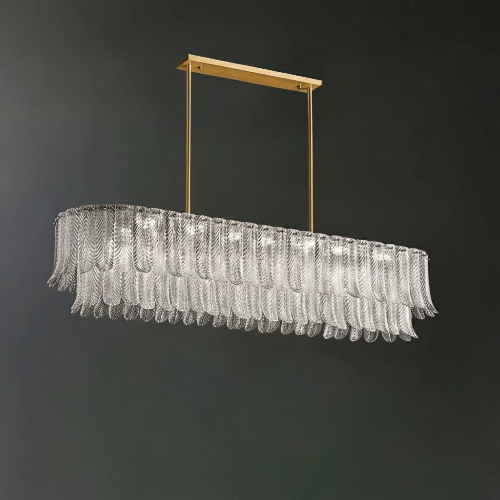 A Clérachic linear pendant of clear glass leaves hangs from a brass bar on two rods, against a dark green-grey wall.