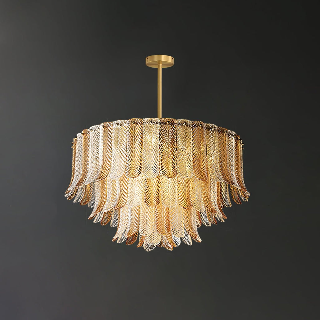 A lit Clérachic pendant of layered glass leaves hangs from a brass rod, the clear glass picking up a warm amber glow.