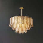 A lit Clérachic pendant of layered glass leaves hangs from a brass rod, the clear glass picking up a warm amber glow.