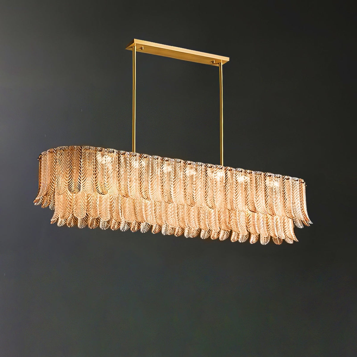A lit Clérachic linear pendant with amber glass leaves glows warm below a brass bar, against a dark grey backdrop.