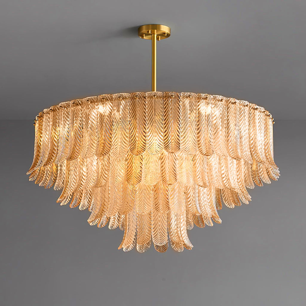 A wide, lit Clérachic pendant of amber glass leaves in tiers hangs from a brass rod and round ceiling plate on grey.