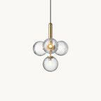 Clérachic pendant with four clear textured glass globes on a brass rod, shown lit against a plain white backdrop.