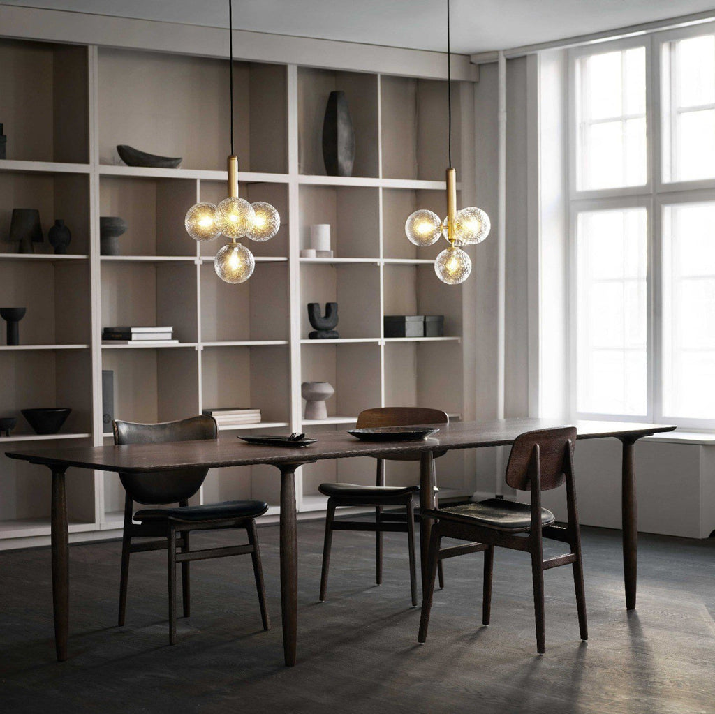 Two Clérachic cluster pendants with clear glass globes hang beside tall white shelving over a dark wood dining table.
