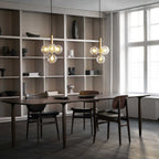 Two Clérachic cluster pendants with clear glass globes hang beside tall white shelving over a dark wood dining table.
