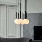 A group of black-rod Clérachic pendants with white opal globes hangs before a panelled wall and a grey plaster fireplace.