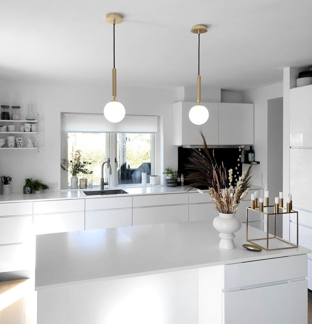 Two single-globe brass-rod pendants from Clérachic with white opal glass hang above a white kitchen island.