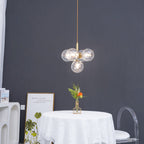 A gold-rod Clérachic cluster pendant with clear glass globes hangs against a dark grey wall above a white-clothed table.