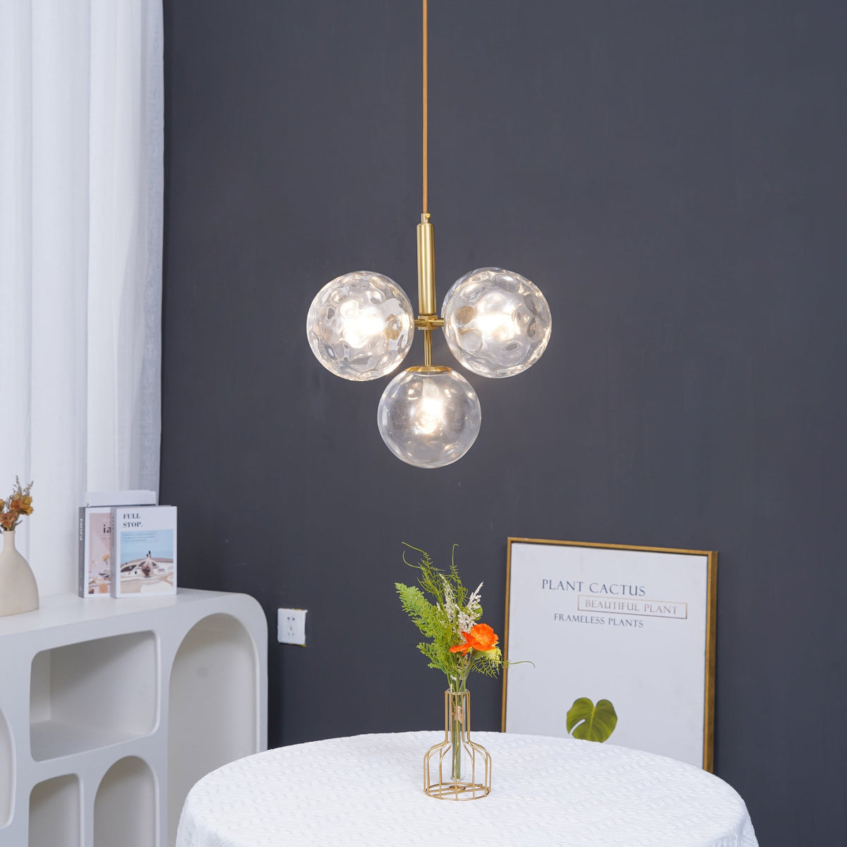 Three-globe Clérachic pendant in clear rippled glass, lit warm, with a vase of flowers and a framed print below.