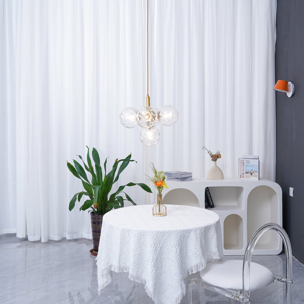 Distant view of a gold-rod Clérachic cluster pendant beside an orange wall light, with a plant and round table below.