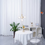 Distant view of a gold-rod Clérachic cluster pendant beside an orange wall light, with a plant and round table below.