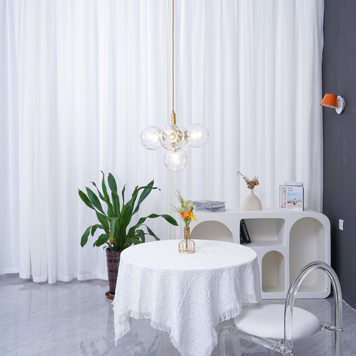 Distant view of a gold-rod Clérachic cluster pendant beside an orange wall light, with a plant and round table below.