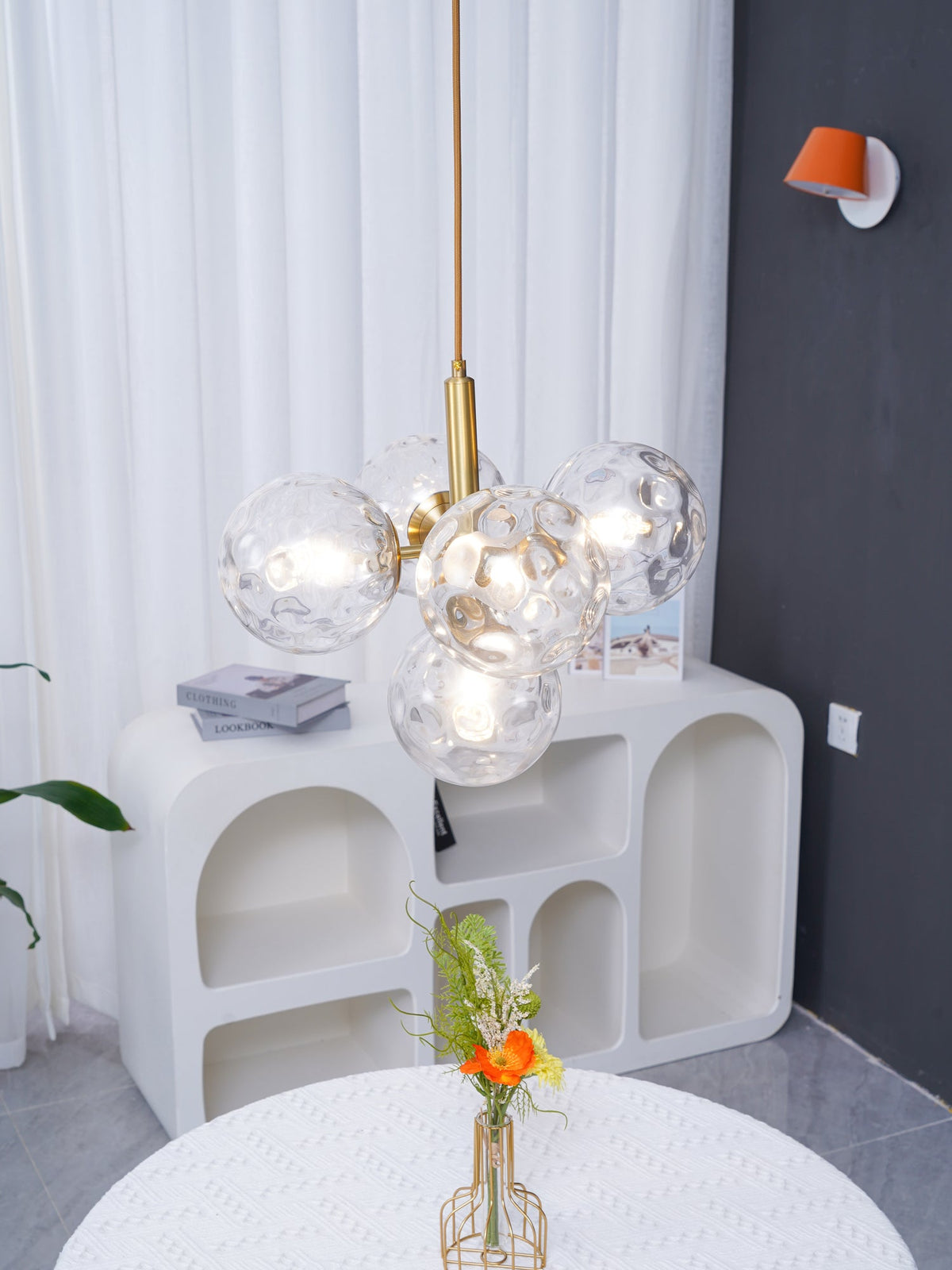 Clear, rippled glass cluster pendant from Clérachic with a gold rod, seen close up above a white arched console.