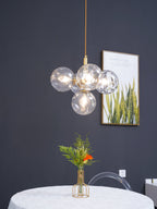 Gold-rod Clérachic cluster pendant with clear rippled globes and a lit bulb, hanging against a dark grey wall.