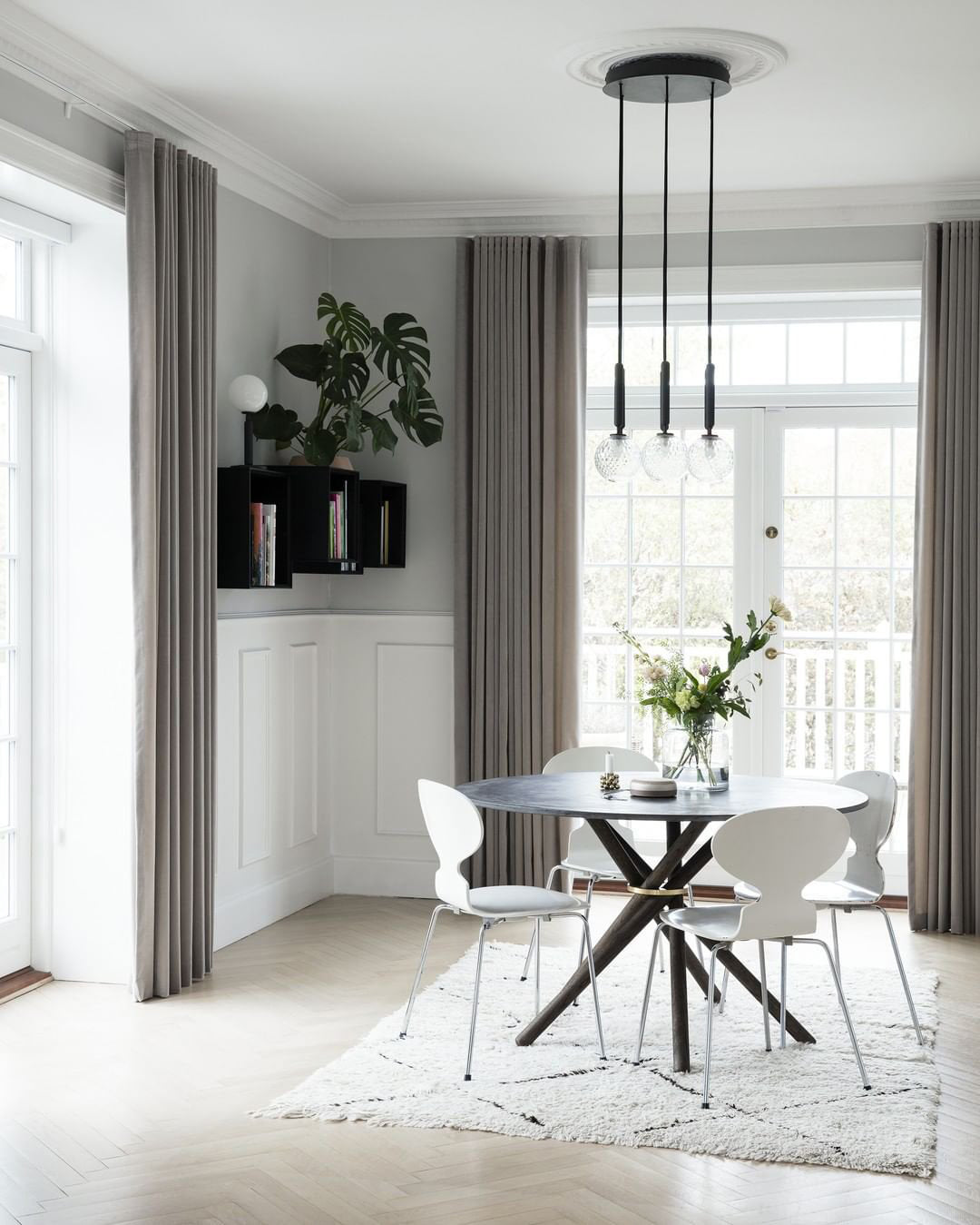 Three-head black Clérachic pendant on a round ceiling plate, hung over a round table by a tall French window.