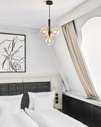 Clear-glass cluster pendant from Clérachic with a black rod, hanging in a bedroom under a sloped white ceiling.