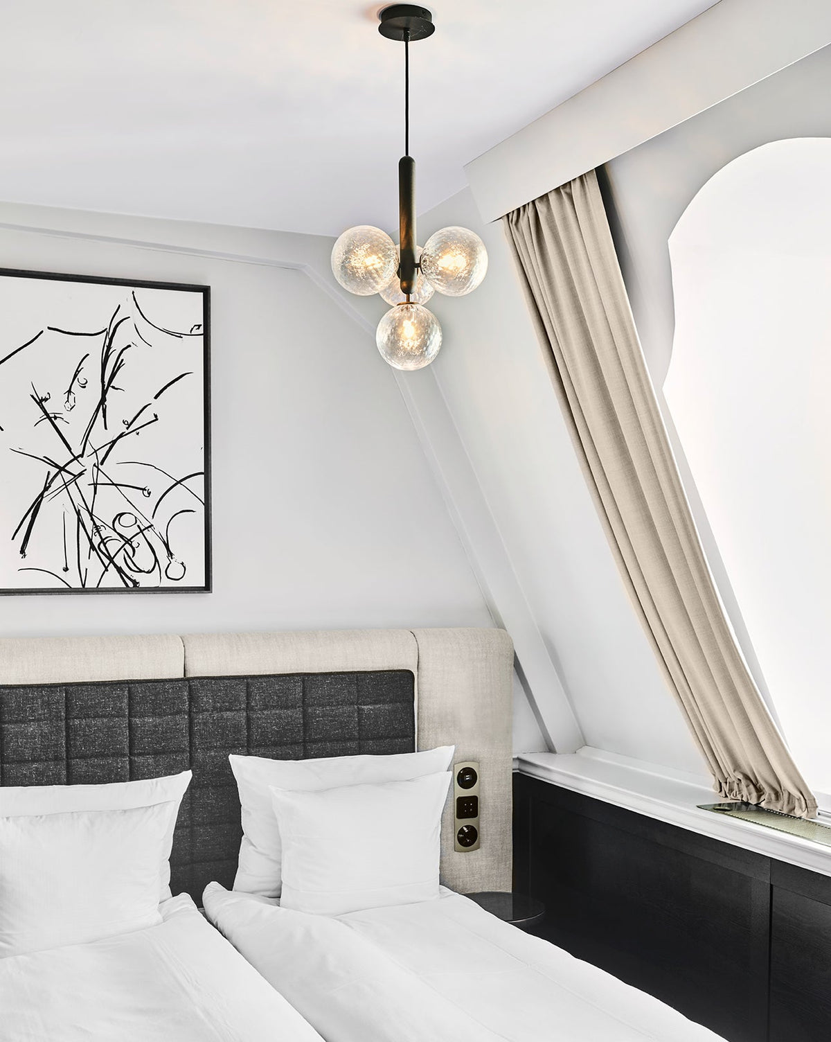 Clear-glass cluster pendant from Clérachic with a black rod, hanging in a bedroom under a sloped white ceiling.