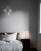Clear glass cluster pendant from Clérachic hangs above a bed with grey linen and a small brass table lamp.