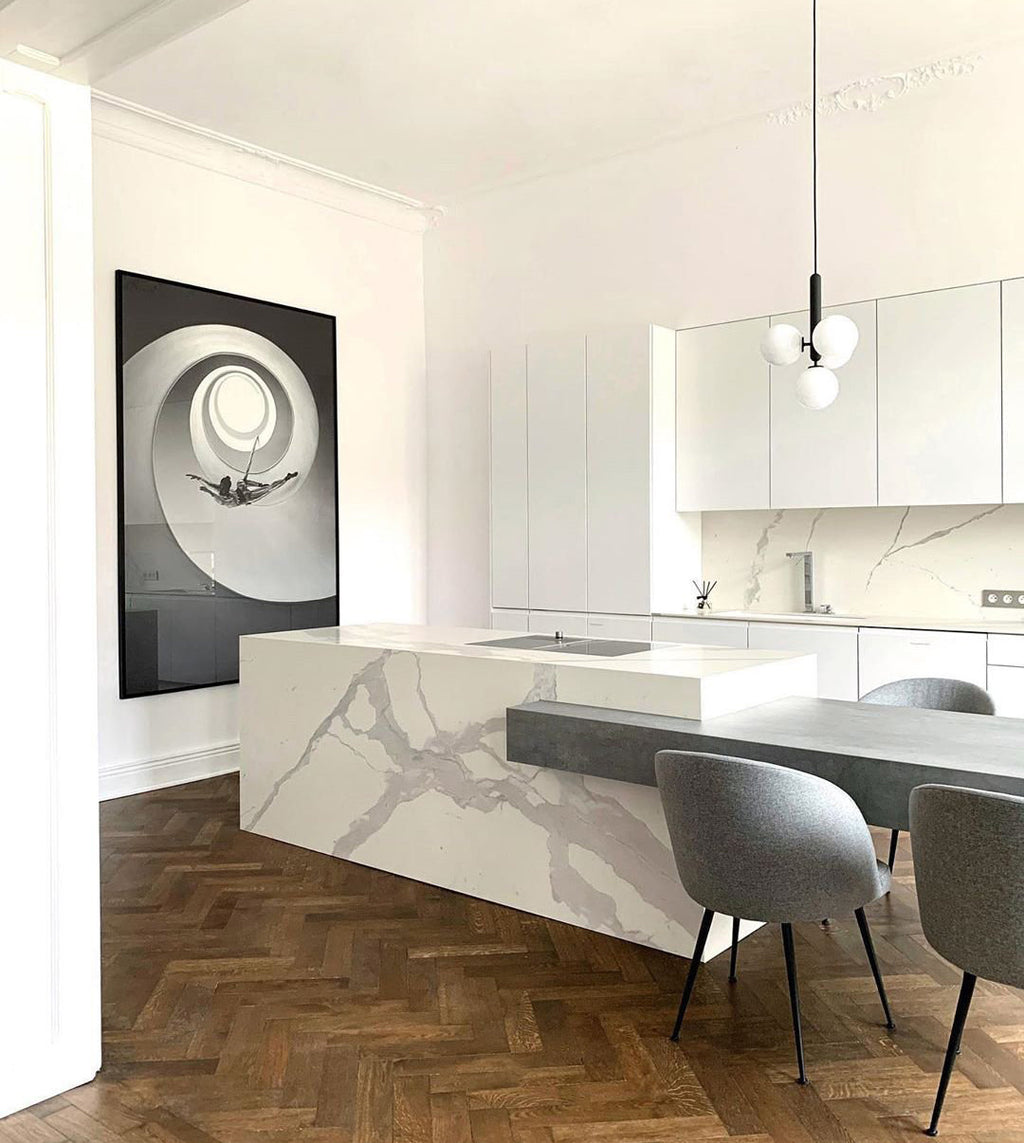 Small Clérachic cluster pendant with white globes hangs over a marble kitchen island beside grey velvet chairs.